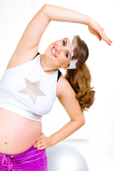 Улыбающаяся красивая беременная женщина делает упражнения в гостиной — стоковое фото