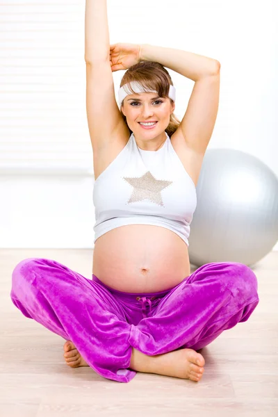 Uśmiechający się piękna kobieta w ciąży co gimnastyka w salonie — Zdjęcie stockowe