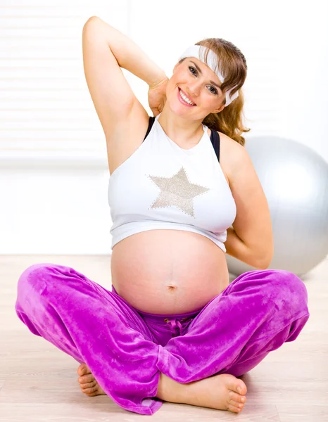Улыбающаяся красивая беременная женщина делает гимнастику в гостиной — стоковое фото
