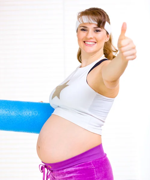Jest yukarı gösteren egzersiz minderi ile gülümseyen güzel bir hamile kadın — Stok fotoğraf