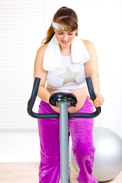 Beautiful pregnant female training on exercise bike — Stock Photo, Image