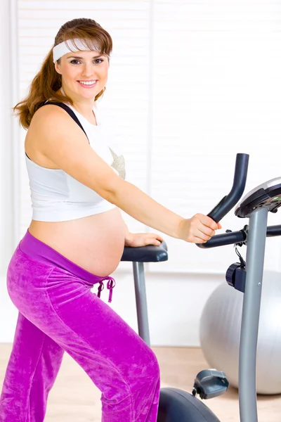 Vackra gravid kvinna utbildning på motionscykel — Stockfoto