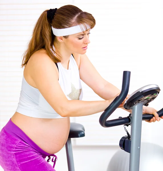 Beautiful pregnant female training on exercise bike — Stock Photo, Image