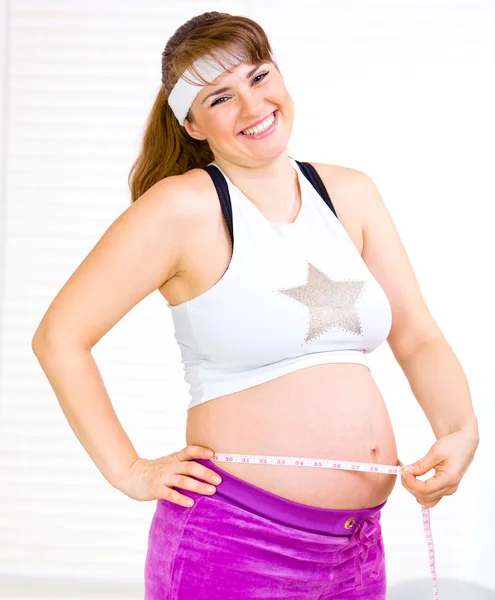 Laughing beautiful pregnant woman measuring belly — Stock Photo, Image