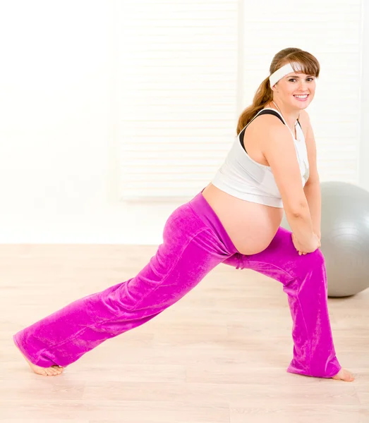 Sonriendo hermosa embarazada haciendo ejercicios de estiramiento en casa — Foto de Stock