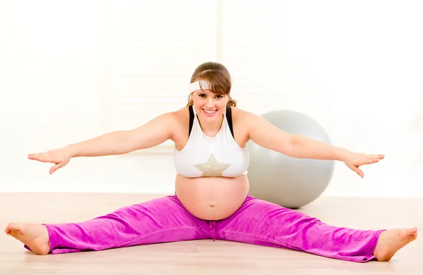 Улыбающаяся красивая беременная женщина делает упражнения на растяжку дома — стоковое фото