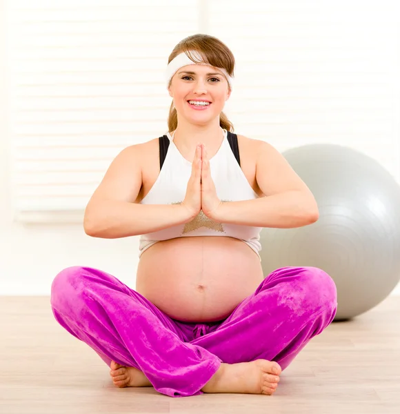 Sonriendo hermosa mujer embarazada haciendo ejercicios de yoga en el suelo en casa — Foto de Stock