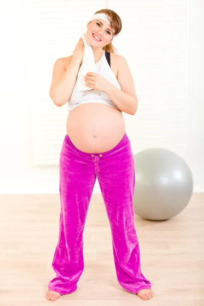 Mujer embarazada sonriente limpiándose la cara con toalla después de hacer ejercicio en casa —  Fotos de Stock