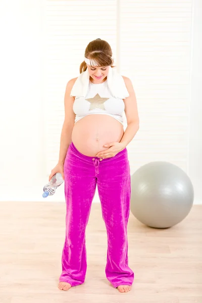 Беременная женщина в спортивной одежде держит бутылку воды и смотрит на живот — стоковое фото