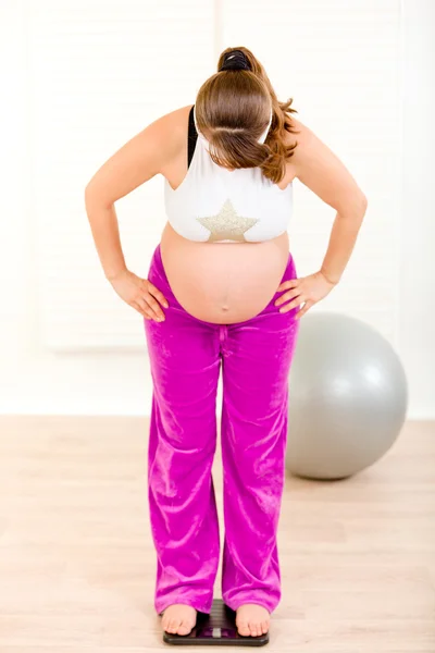 Беременная женщина, стоящая на весах дома — стоковое фото