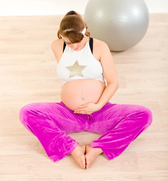 Těhotná žena v sportovní sedí na podlaze a drží jí břicho — Stock fotografie
