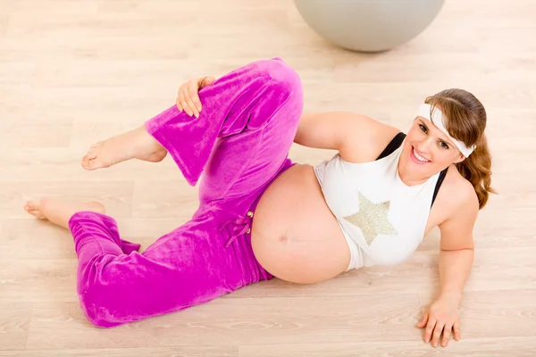 Sorrindo bela fêmea grávida fazendo exercícios de alongamento em casa — Fotografia de Stock