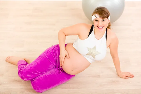 Усміхнена красива вагітна жінка сидить на підлозі і розслабляється — стокове фото