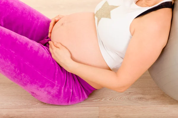 Беременная женщина сидит на полу и расслабляется после тренировки. Крупный план . — стоковое фото