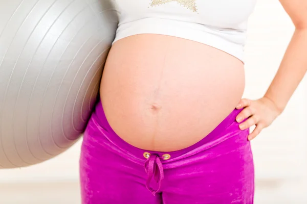 Беременная женщина в спортивной форме держит фитнес-мяч. Крупный план . — стоковое фото