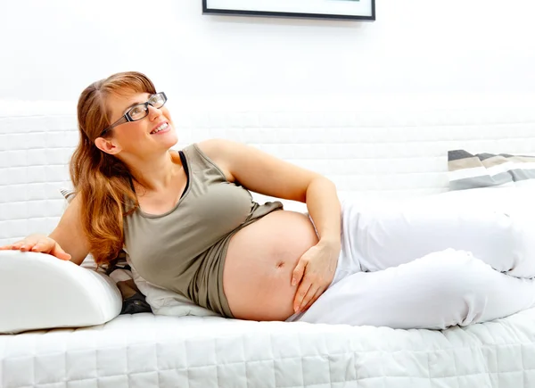 Sonriendo hermosa mujer embarazada acostada en el sofá y sosteniendo su vientre —  Fotos de Stock