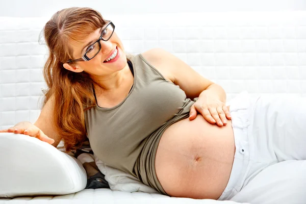 Sorrindo bela fêmea grávida relaxando no sofá e segurando sua barriga . — Fotografia de Stock