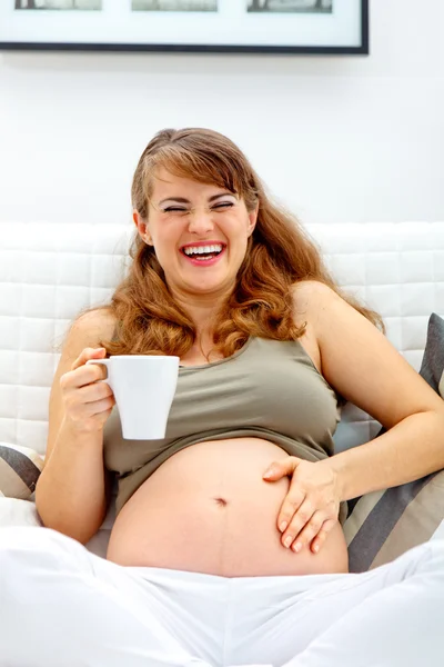 Śmiejąc się piękna kobieta w ciąży, siedząc na kanapie — Zdjęcie stockowe
