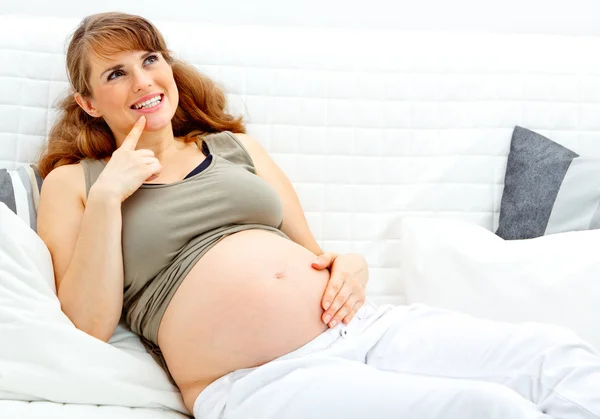 Όνειρα όμορφη έγκυος γυναίκα κάθεται στον καναπέ και κρατώντας την κοιλιά — Φωτογραφία Αρχείου