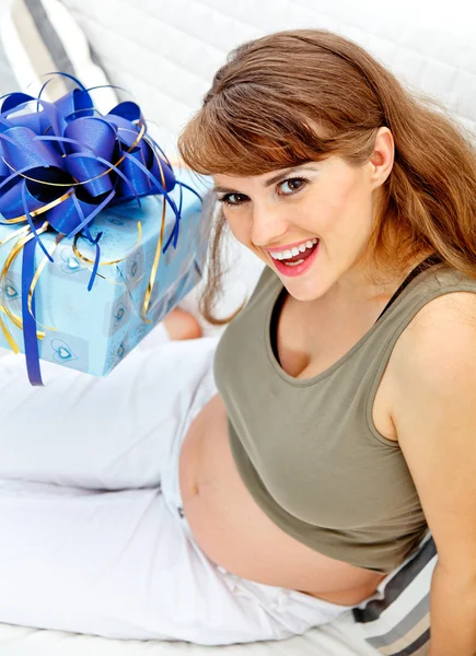 Donna incinta seduta sul divano di casa con regali per il suo bambino non ancora nato — Foto Stock