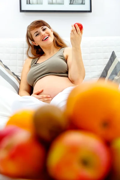 아름 다운 임신한 여자 소파에 편안 하 고 h에 과일을 들고 웃 고 — 스톡 사진