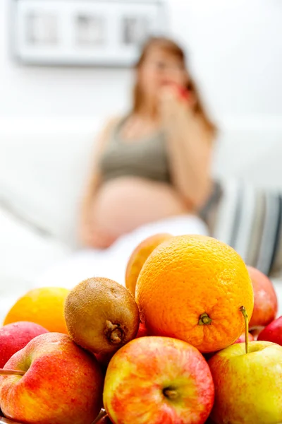 Piatto di frutta sul tavolo e donna incinta seduta sul divano in background — Foto Stock