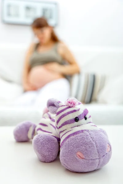 Brinquedo deitado na mesa e mulher grávida sentada no sofá no fundo — Fotografia de Stock