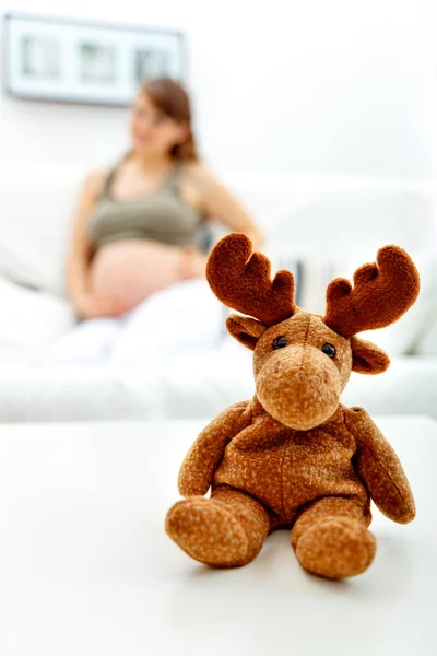 Spielzeug auf Tisch liegend und schwangere Frau auf Sofa im Hintergrund sitzend — Stockfoto