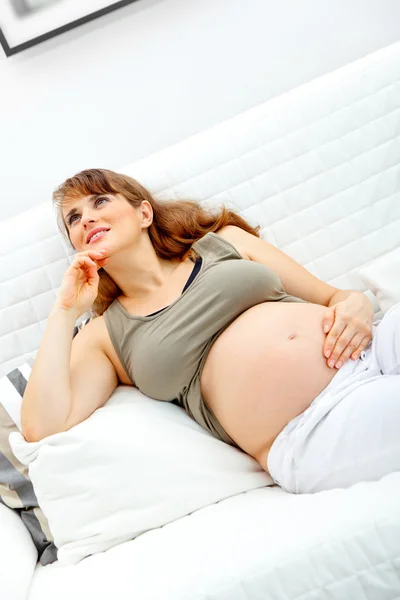 Sueña hermosa mujer embarazada sentada en el sofá y sosteniendo su vientre —  Fotos de Stock