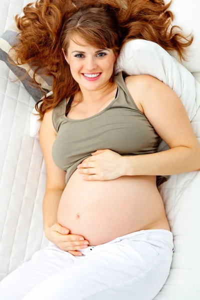 Happy beautiful pregnant woman relaxing on sofa and holding her belly. — Stock Photo, Image