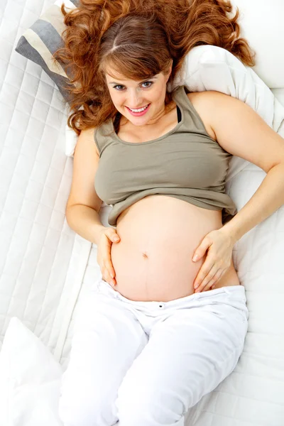 Ευτυχής όμορφη έγκυος γυναίκα χαλάρωση στον καναπέ και κρατώντας την κοιλιά — Φωτογραφία Αρχείου