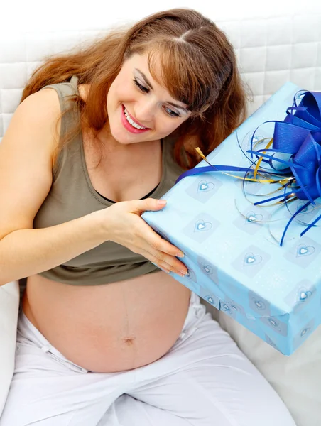 Mulher grávida sentada no sofá com presente para seu bebê por nascer — Fotografia de Stock