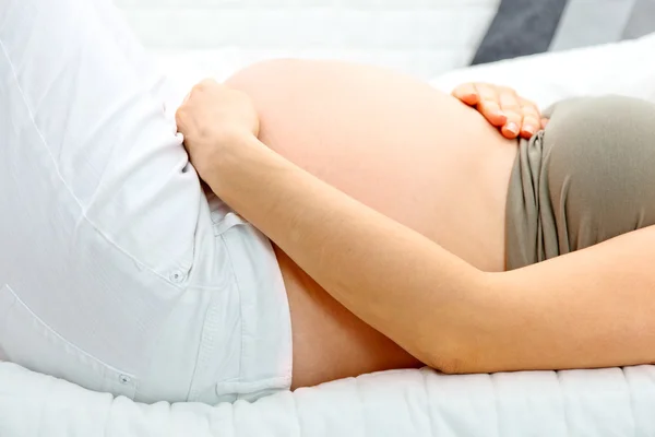 Schwangere liegt auf Sofa und hält ihren Bauch. Nahaufnahme. — Stockfoto