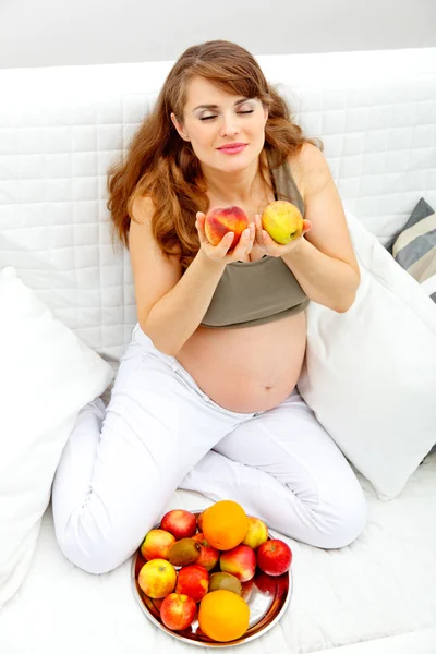Красивая беременная женщина сидит на диване и наслаждается фруктами — стоковое фото
