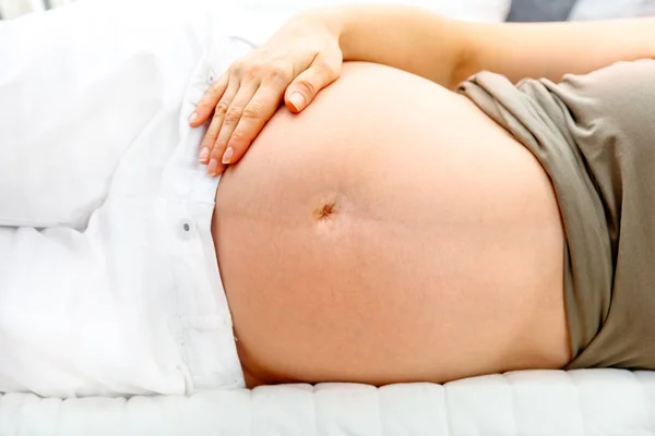 Έγκυος γυναίκα ξαπλωμένη στον καναπέ και κρατώντας την κοιλιά. κινηματογράφηση σε πρώτο πλάνο. — Φωτογραφία Αρχείου