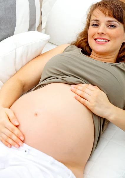 아름 다운 임신한 여자 소파에 편안 하 고 그녀의 아랫 배를 잡고 웃 고 — 스톡 사진