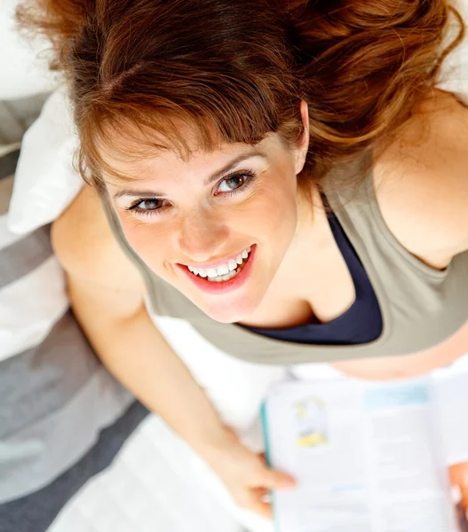 Sorrindo bela mulher grávida sentada no sofá com revista . — Fotografia de Stock