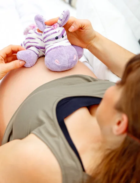 Femme enceinte assise sur un canapé et tenant un jouet sur son ventre . — Photo