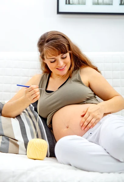 Sonriendo hermosa mujer embarazada tejiendo para su bebé . — Foto de Stock