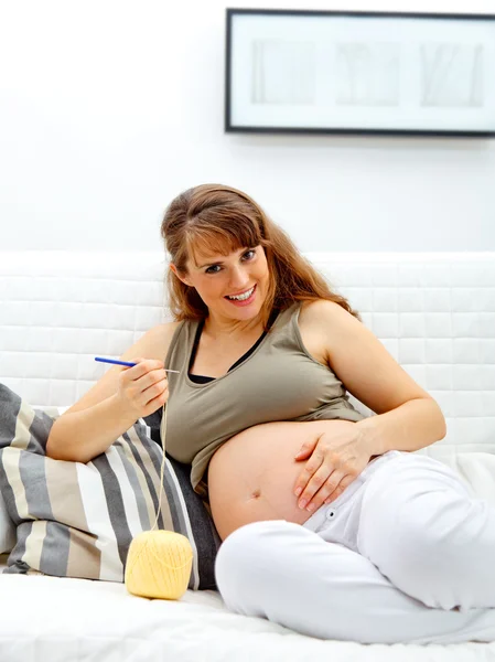 Lächelnde schöne schwangere Frau strickt für ihr Baby. — Stockfoto