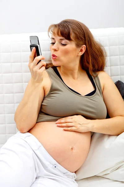 Sorrindo bela mulher grávida sentada no sofá e falando telefone celular . — Fotografia de Stock