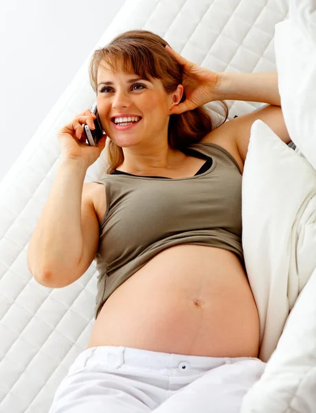 Улыбающаяся красивая беременная женщина сидит на диване и разговаривает по мобильному телефону . — стоковое фото