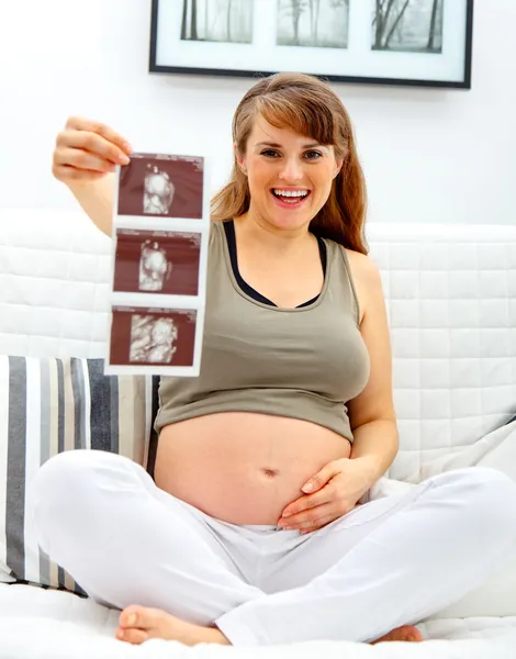 Sonriendo hermosa mujer embarazada sentada en diván con eco en la mano . —  Fotos de Stock