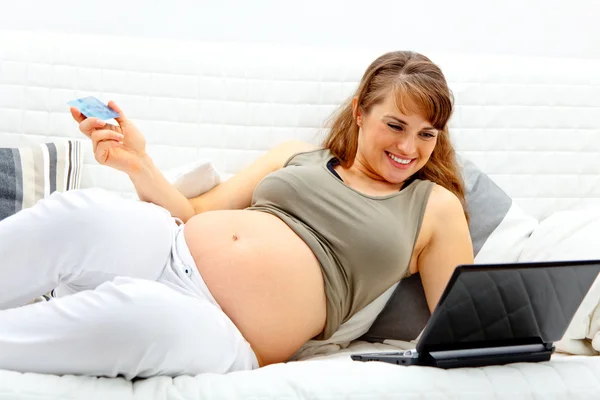 Посміхаючись красива вагітна жінка використовує кредитну картку в магазин з Інтернету — стокове фото