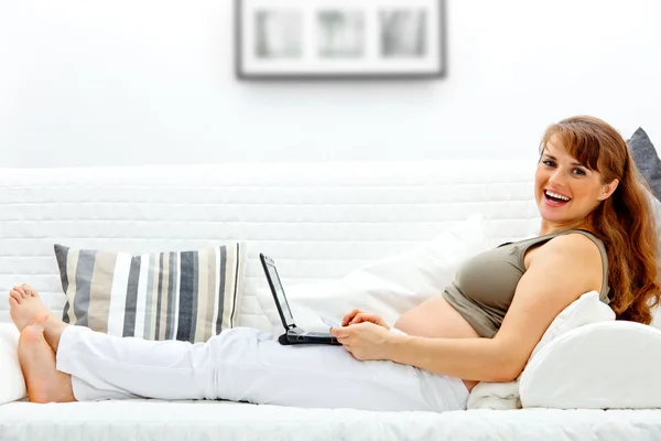Улыбающаяся красивая беременная женщина на диване с ноутбуком и кредиткой — стоковое фото