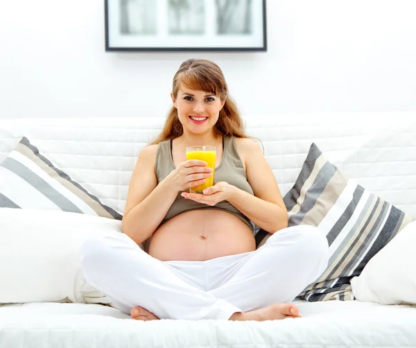 Sorrindo bela mulher grávida sentada no sofá com copo de suco em ha — Fotografia de Stock