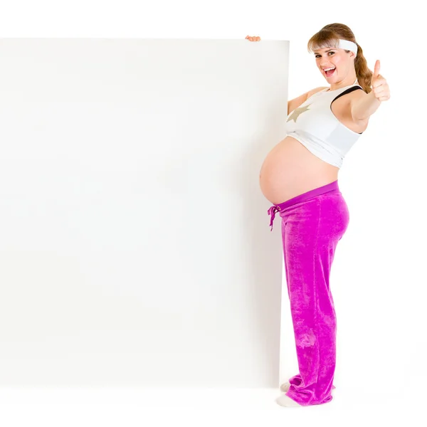 Улыбающаяся красивая беременная женщина держит пустой рекламный щит и показывает большие пальцы — стоковое фото