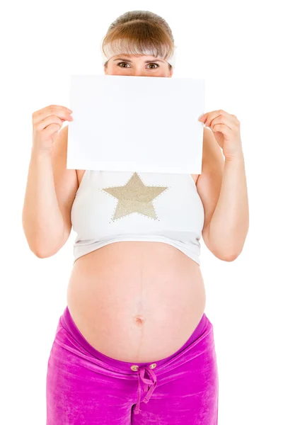 Беременная женщина держит перед лицом пустую белую бумагу — стоковое фото