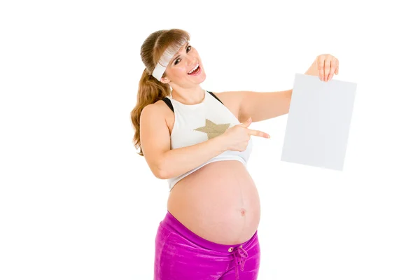 Улыбающаяся красивая беременная женщина указывает пальцем на пустую белую бумагу — стоковое фото