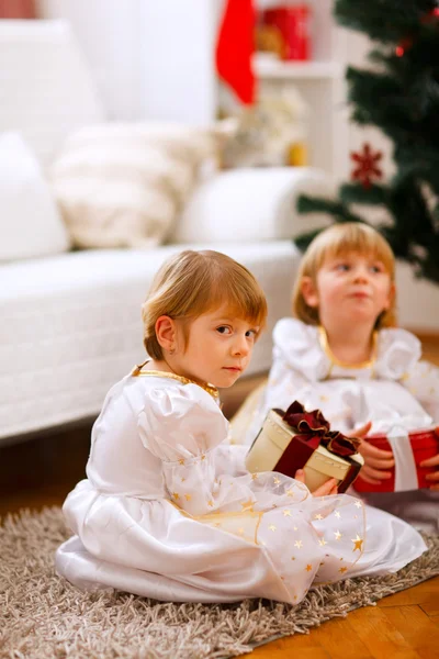 Одна из девочек-близнецов, сидящая с подарком с серьезным выражением — стоковое фото